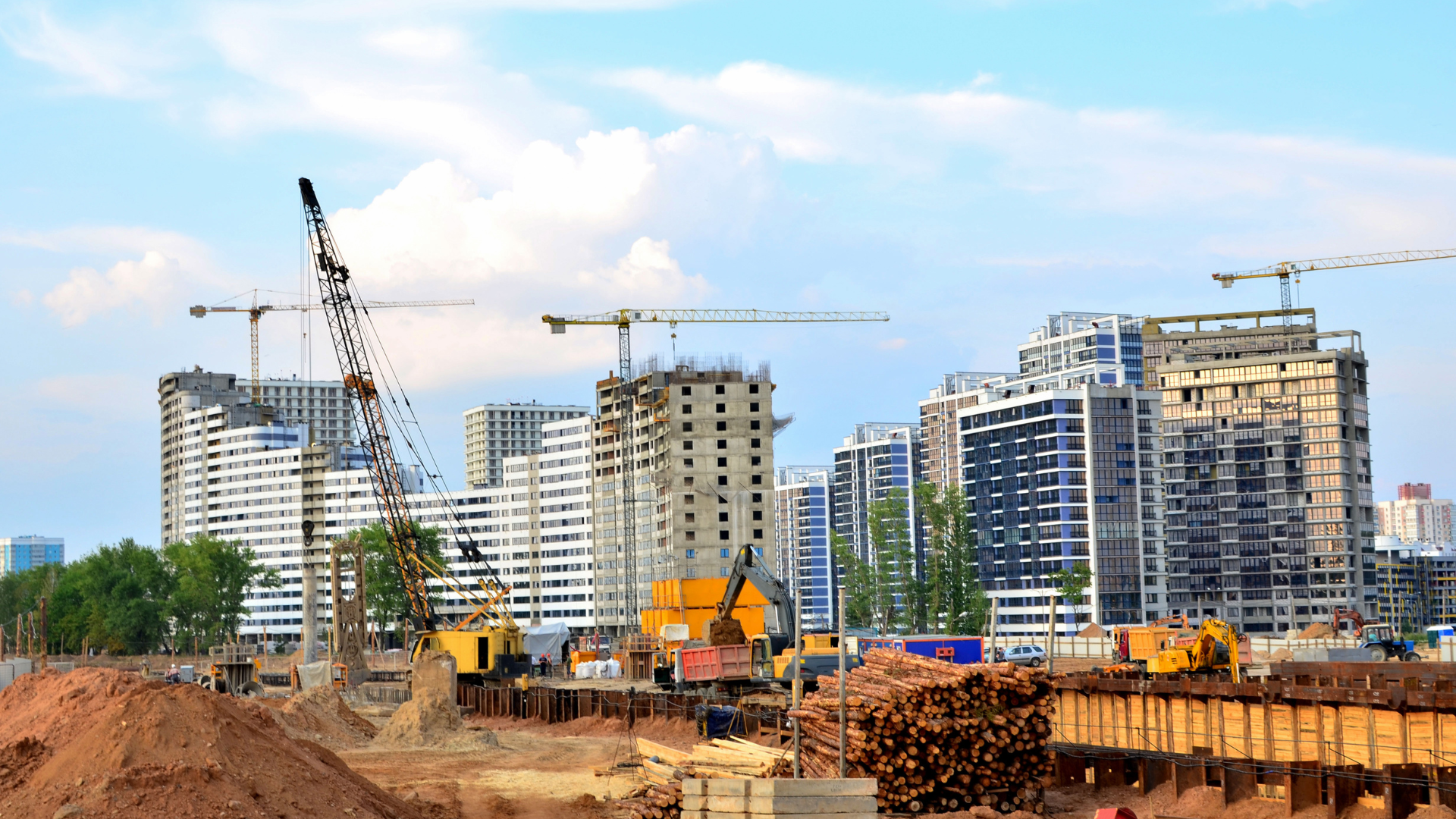 Construction site with multiple high-rise buildings under construction; cranes, earth-moving equipment, and sky.