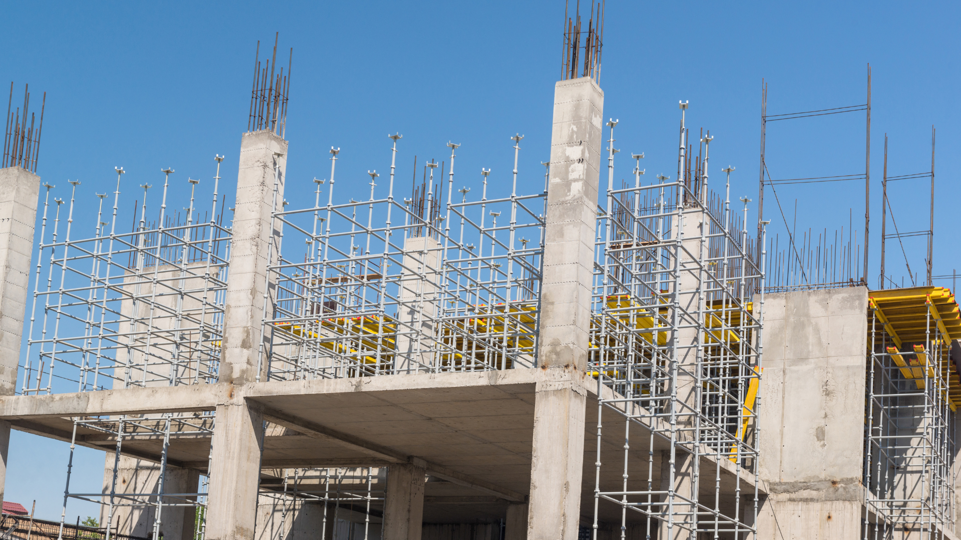 Construction site of a concrete building with exposed rebar and scaffolding under a blue sky.