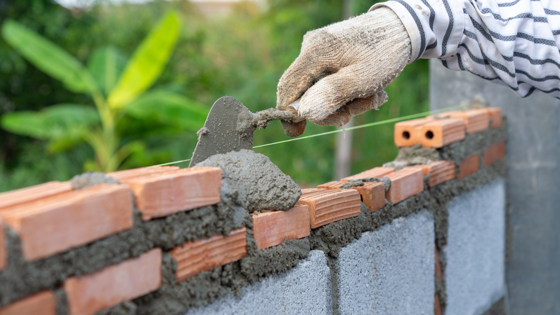 Bricklayer using a trowel to spread mortar on a brick wall during construction, outdoors.