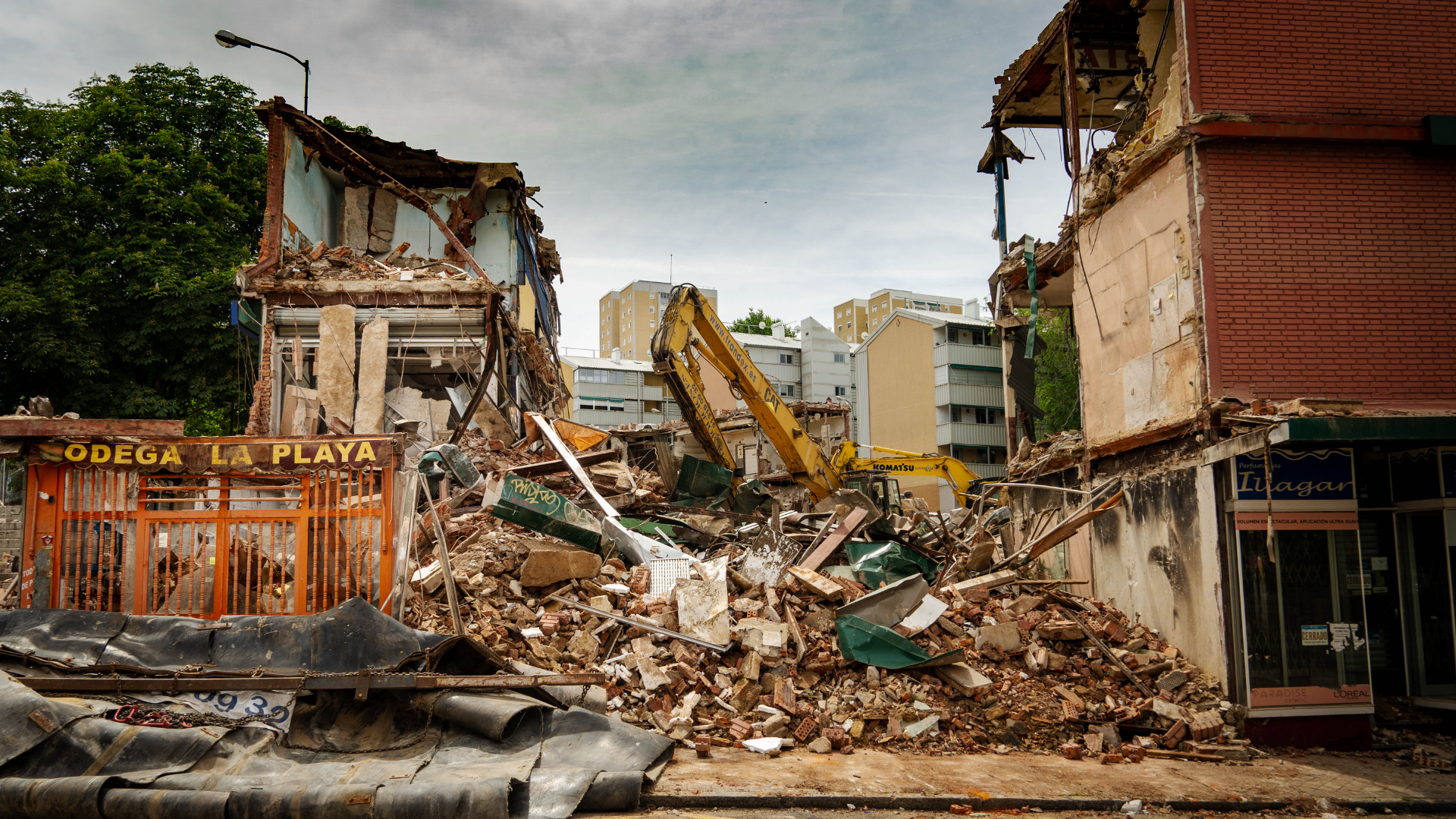 Buildings demolished by heavy machinery, rubble, in an urban setting.