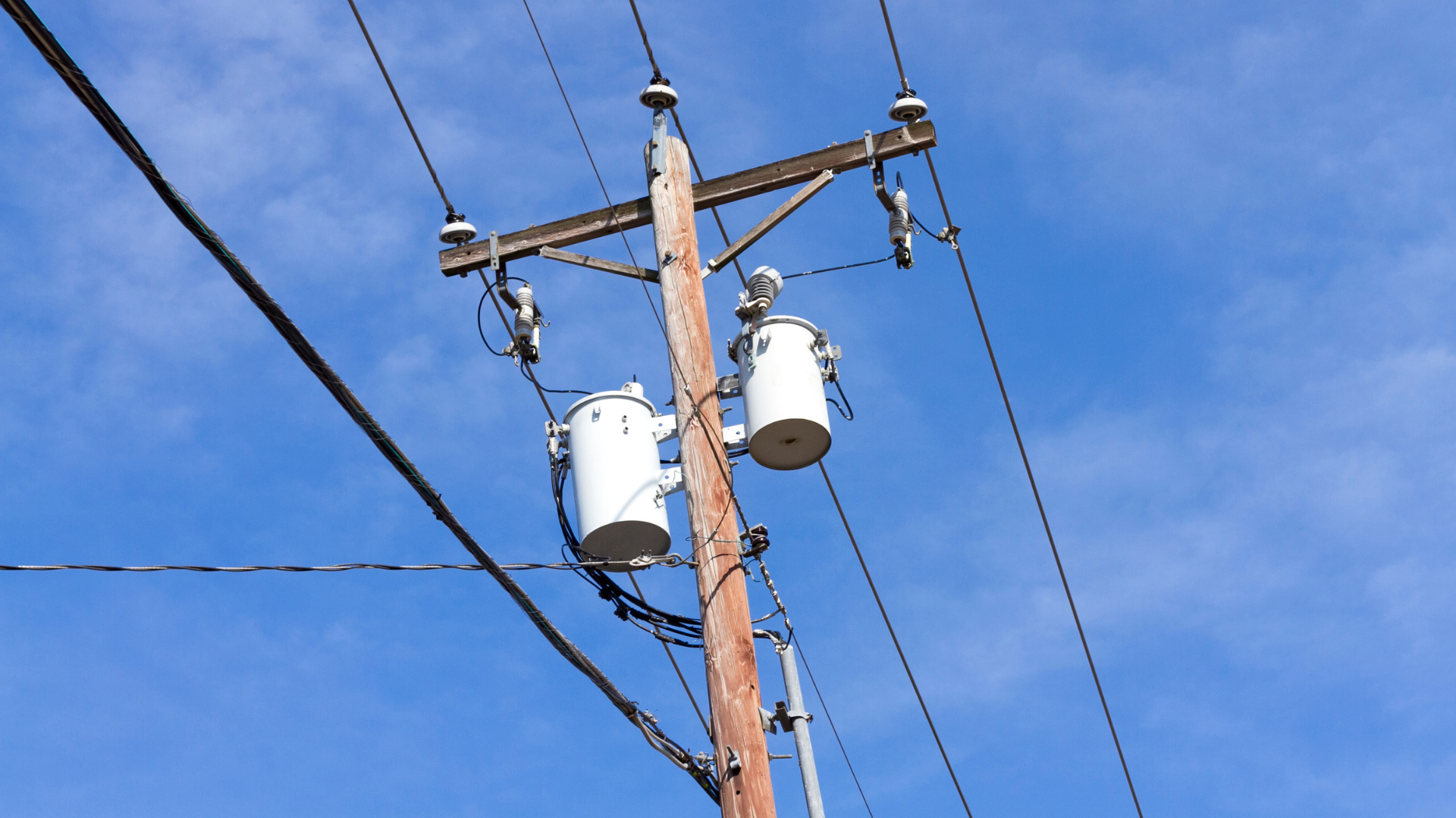 Power lines and transformers on a wooden utility pole against a blue sky.