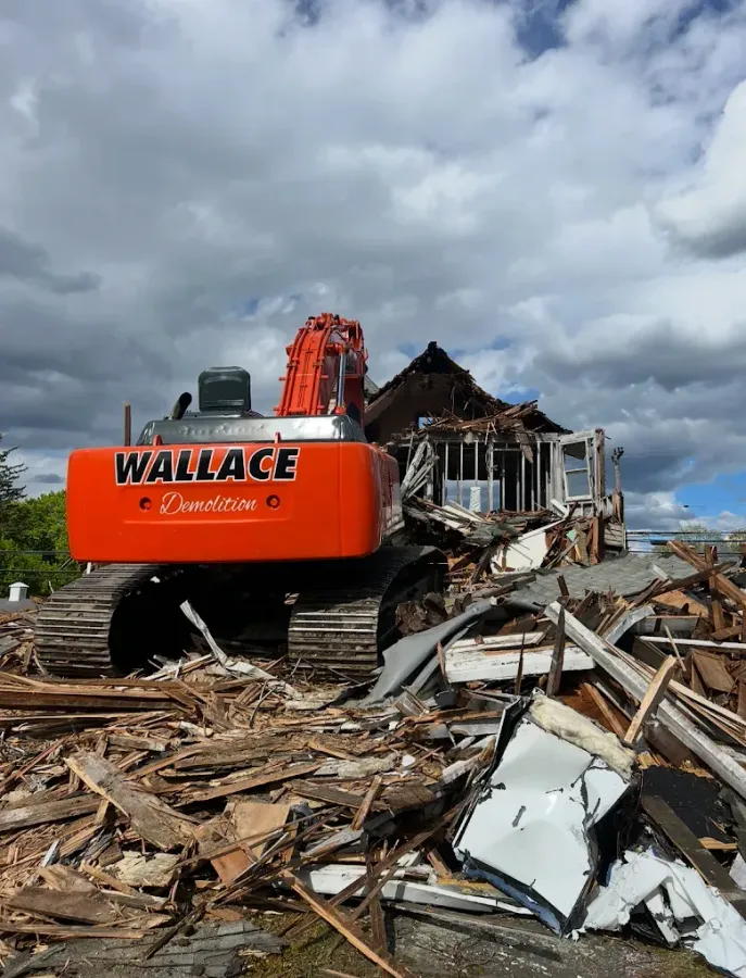 Orange excavator demolishing a building under a cloudy sky. Debris surrounds the machine.