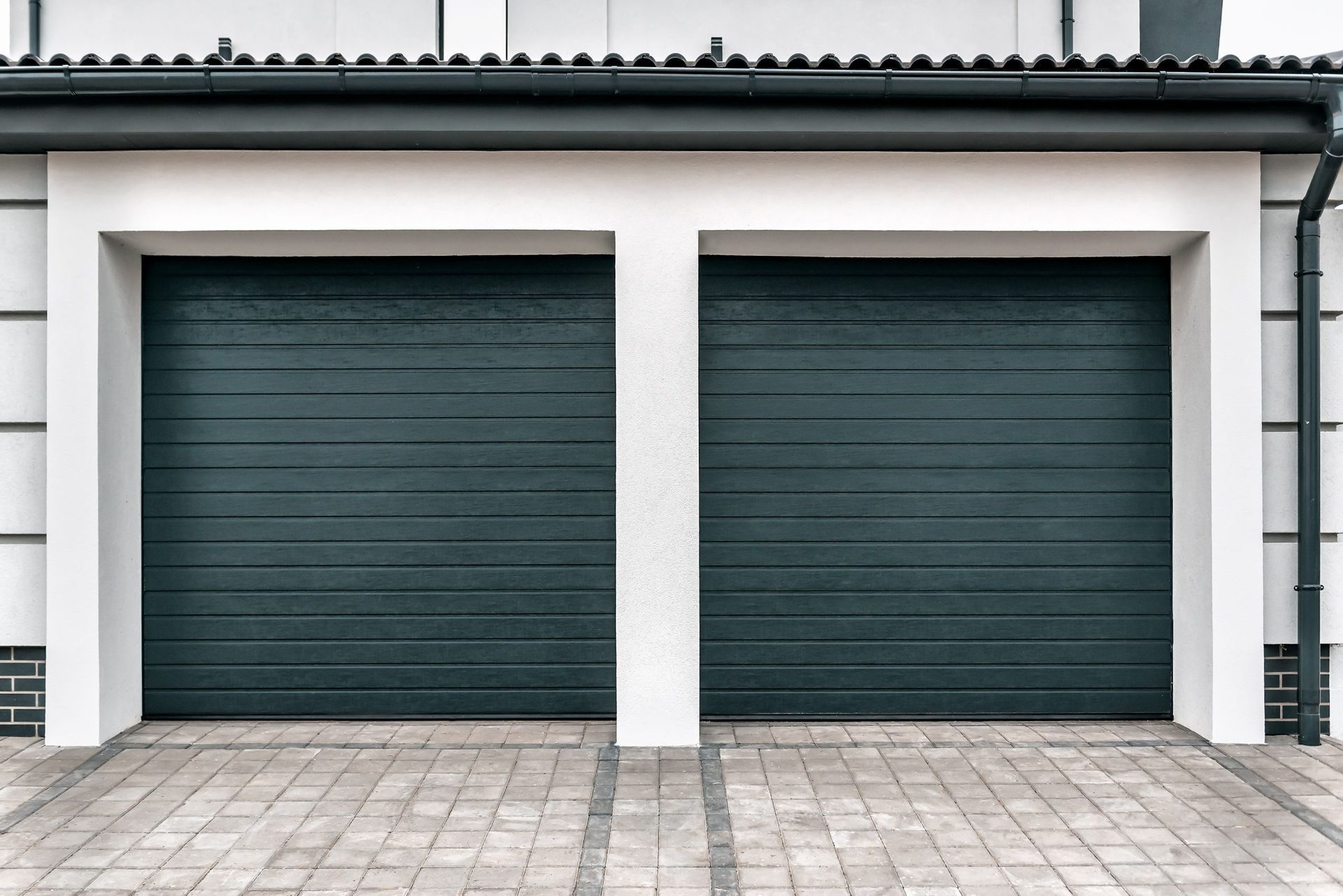 Two dark teal garage doors with white trim, on a brick driveway