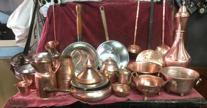 Una collezione di pentole, brocche e recipienti decorativi in ​​rame lucidato, esposti su una superficie di stoffa rosso scuro.
