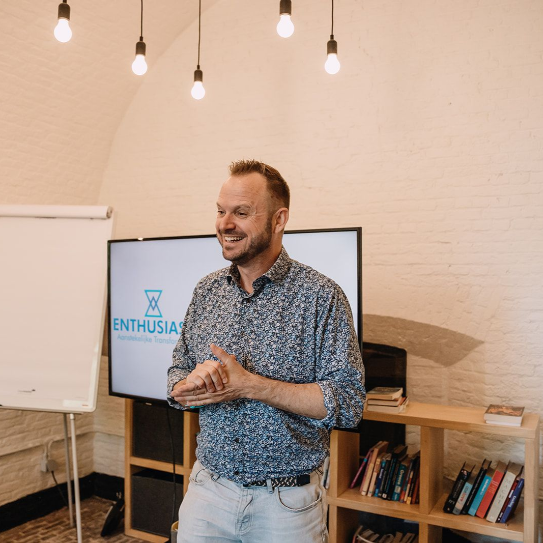 Mensen kijken naar een scherm met de tekst 'Aanstekelijke Transformatie', met een diagram van persoonlijke, sociale en organisatorische transformatie.