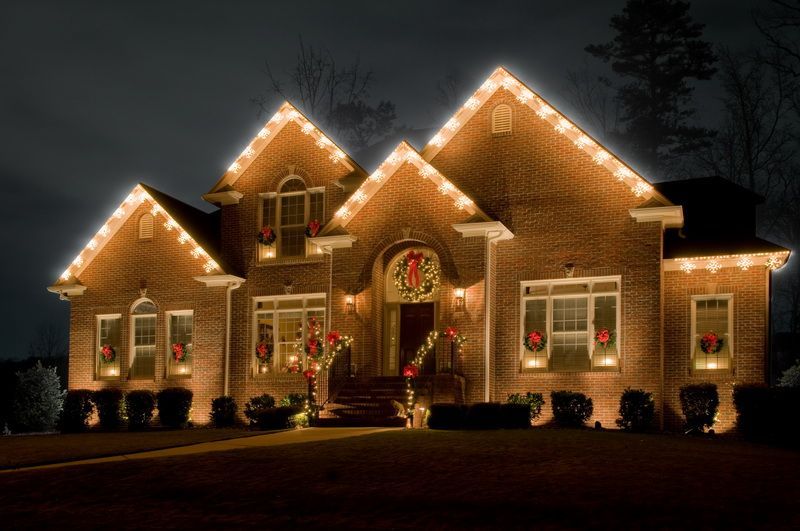 A large brick house is decorated with christmas lights at night.