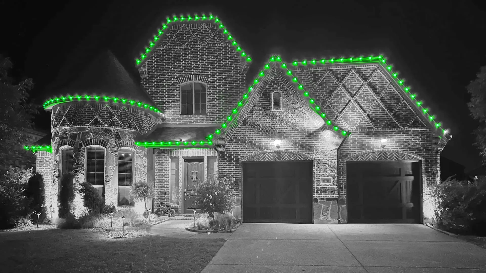 A black and white photo of a house decorated with green christmas lights.