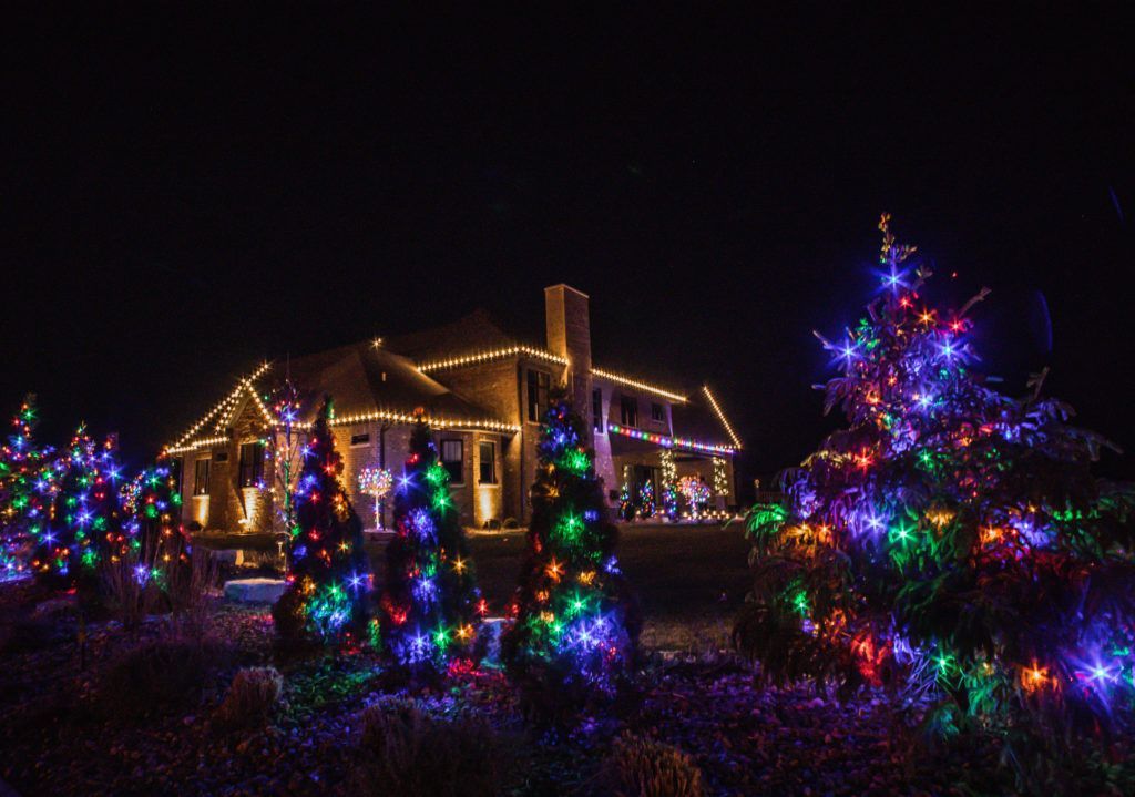 A house is decorated with christmas lights and trees at night.