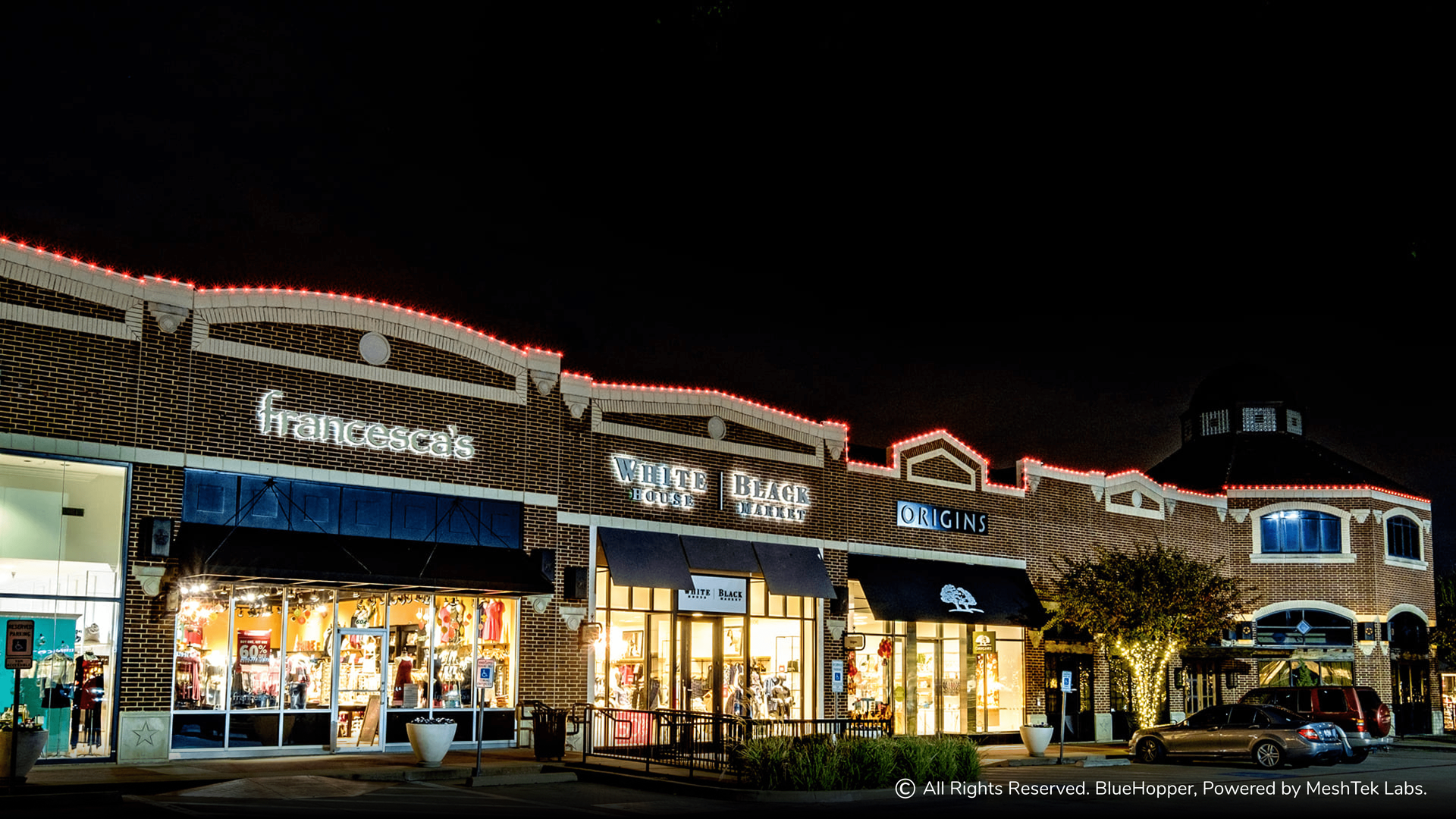 A row of stores are lit up at night with christmas lights.