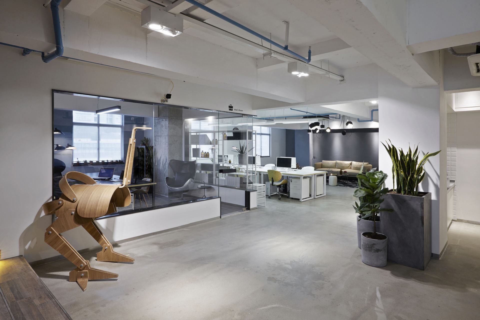 Modern open office interior with desks, glass walls, and a large wooden horse sculpture in the foreground
