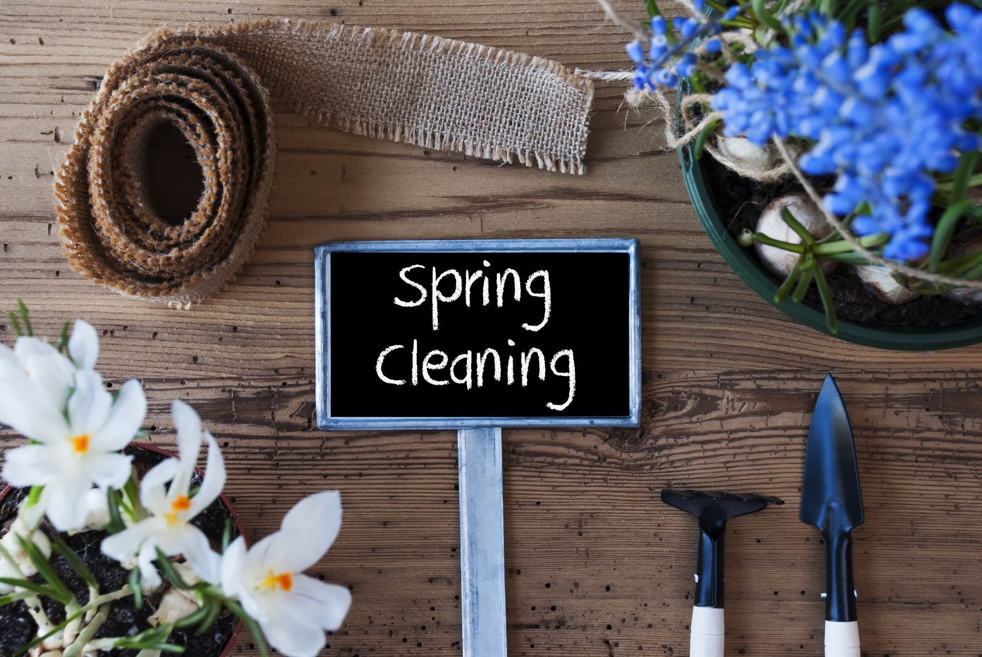 Spring cleaning sign on rustic wood with flowers, burlap roll, and gardening tools