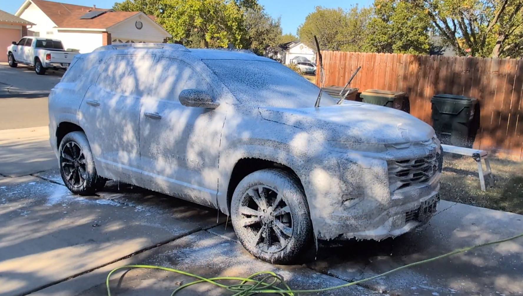 White SUV heavily covered in snow parked in a suburban driveway on a sunny day