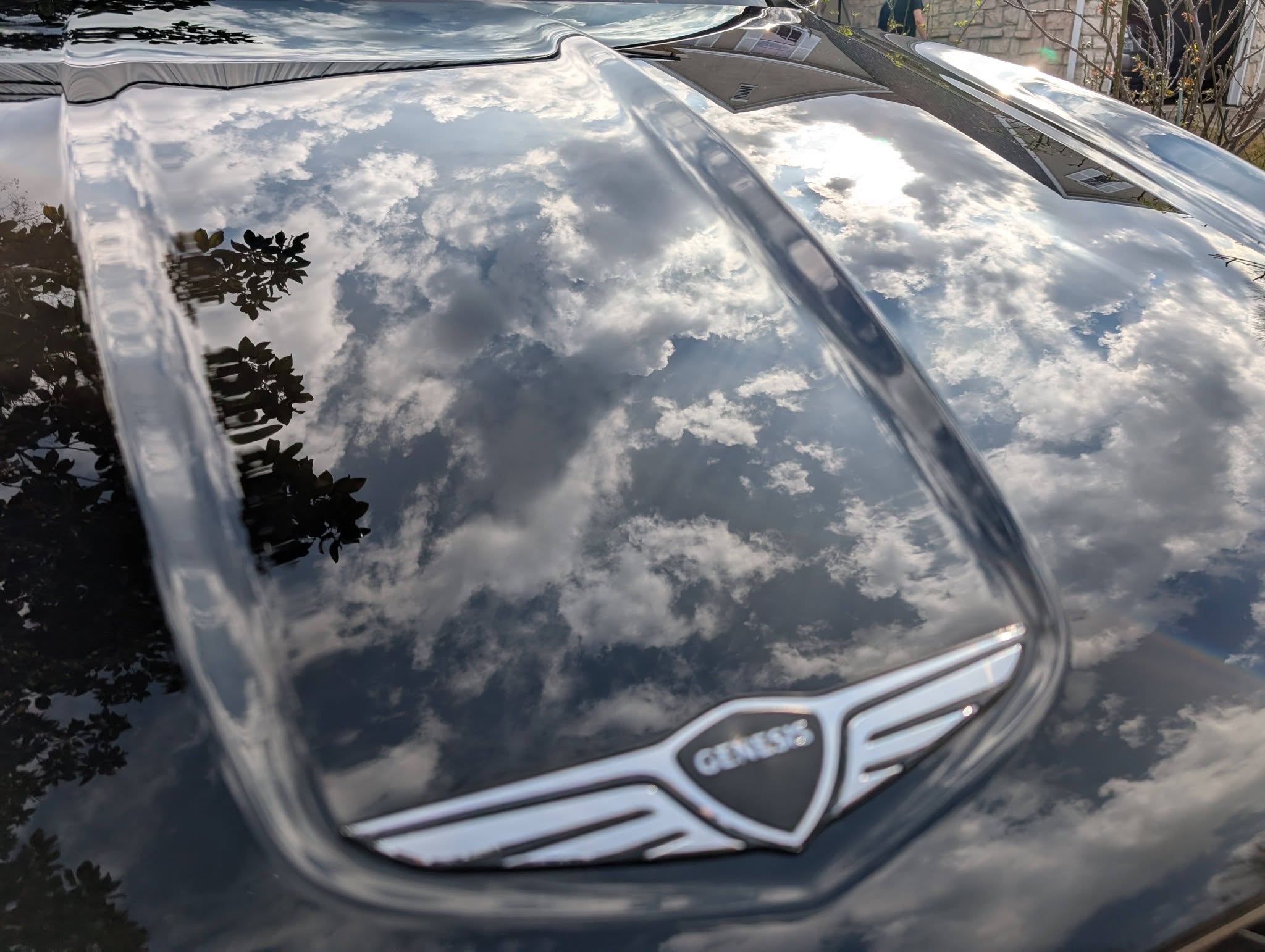 Glossy black car hood reflecting clouds, with a Chrysler emblem centered near the front