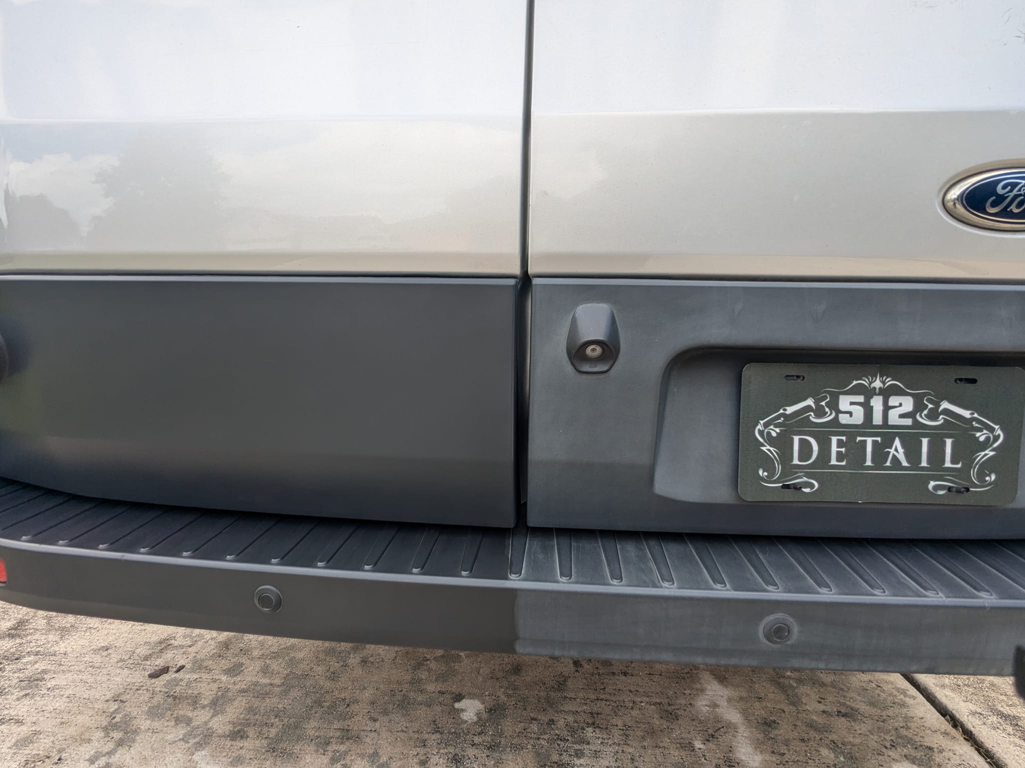 Close-up of a silver van’s rear side with a black step bumper and “Detail” plate frame.