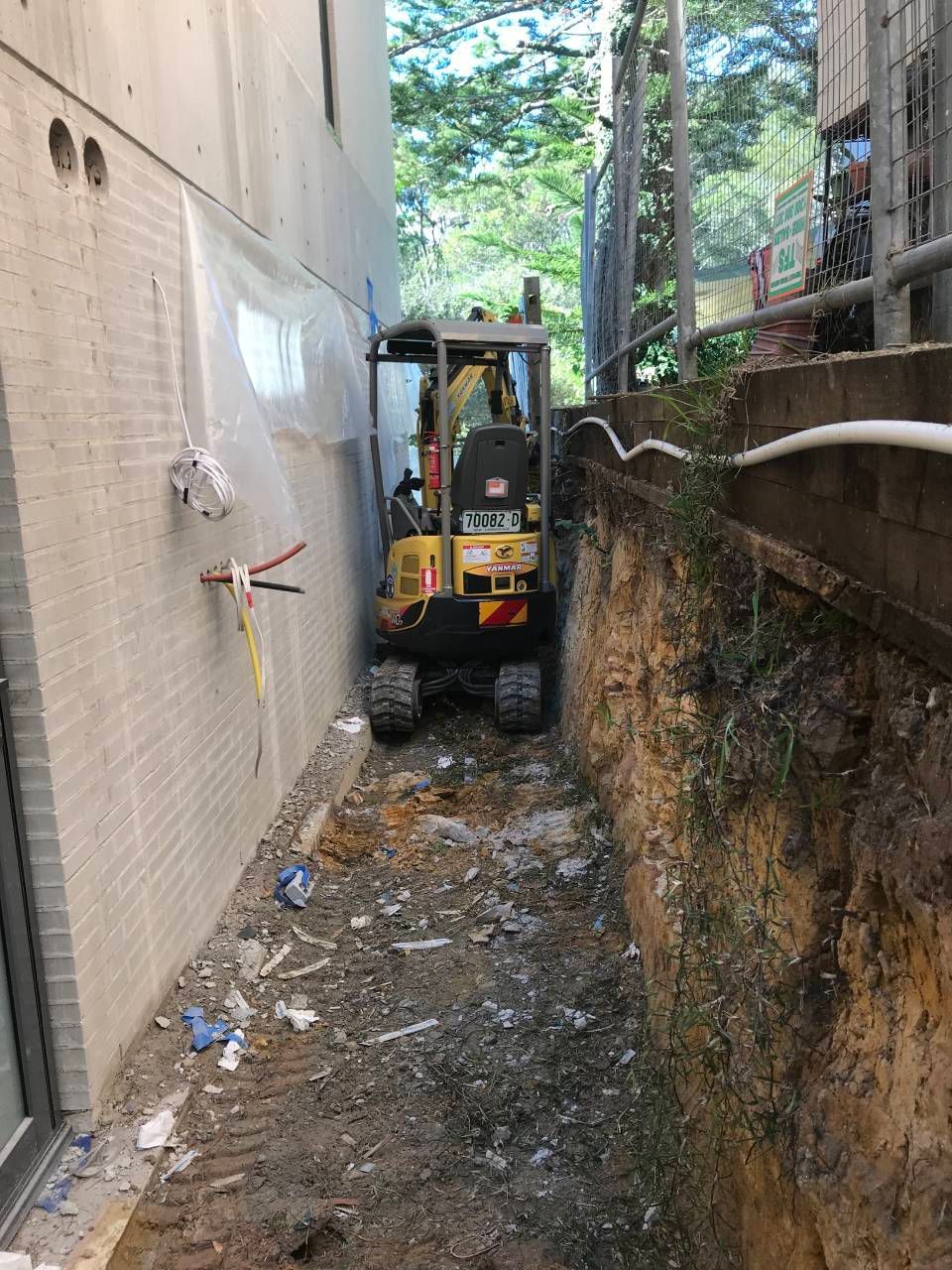 A worker in a high-visibility vest directs an excavator loading dirt into a dump truck at a construction site.