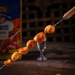 Skewered, spice-coated meatballs on a wooden table with a blurred bottle in the background