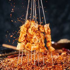 Grilled meat cubes on skewers, coated with spices and sizzling over a bed of red chili flakes