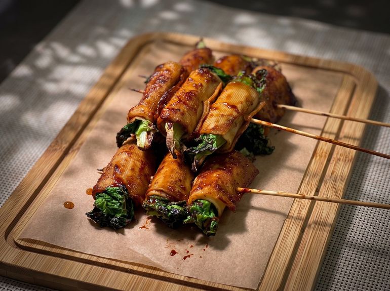 Grilled vegetable skewers on a wooden board, with charred greens and golden-brown wrap