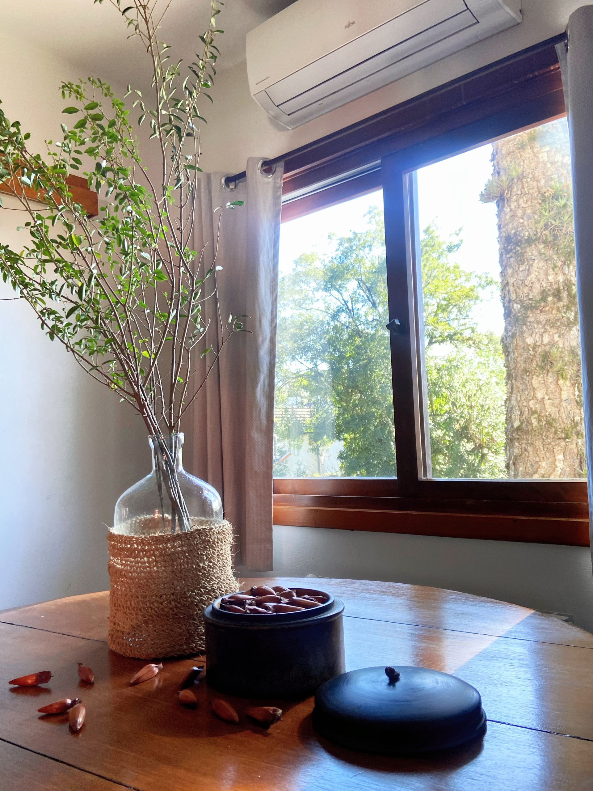 Um vaso de flores está sobre uma mesa de madeira em frente a uma janela.