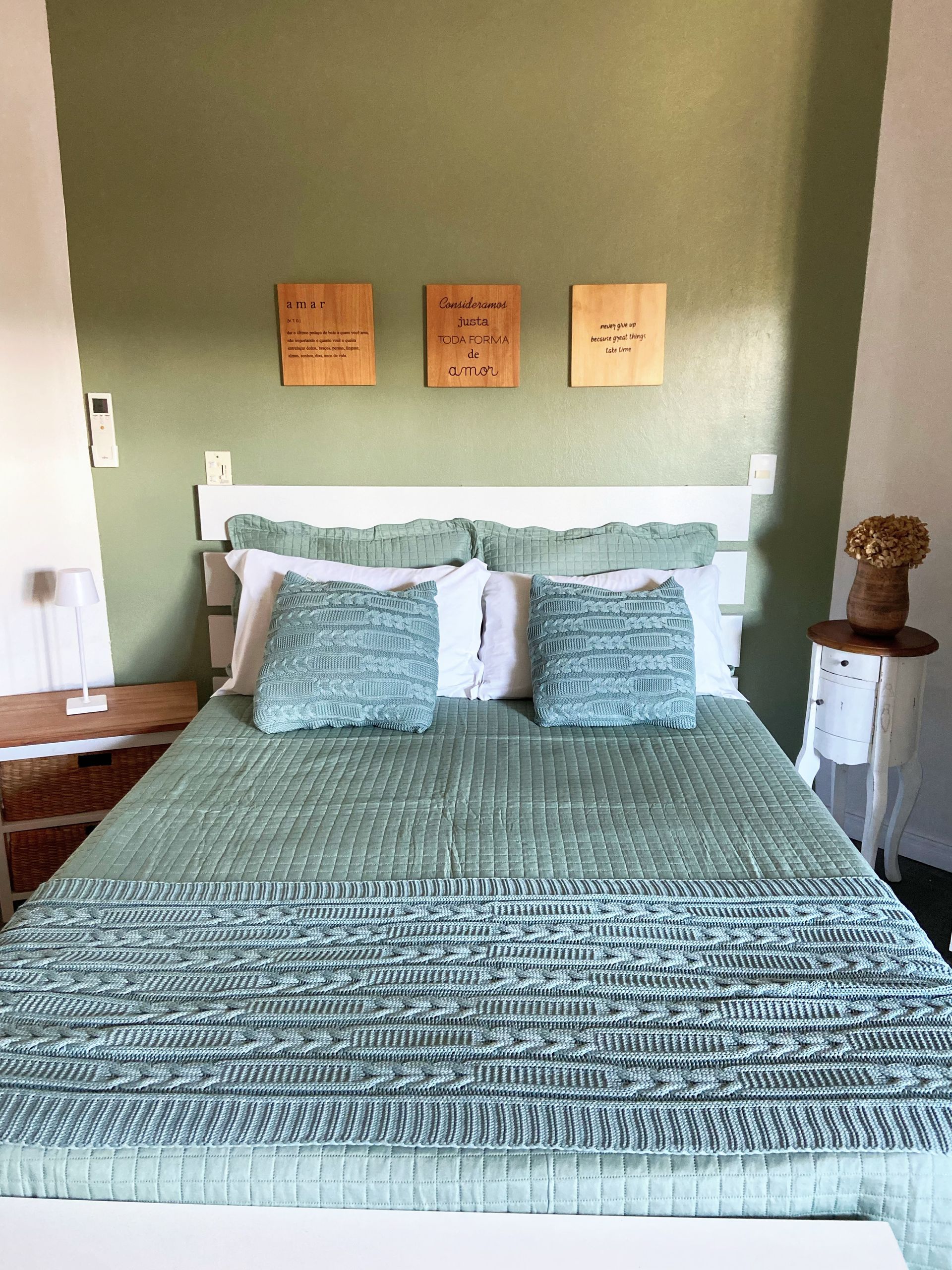 Uma cama com um cobertor verde e travesseiros em um quarto com uma parede verde.