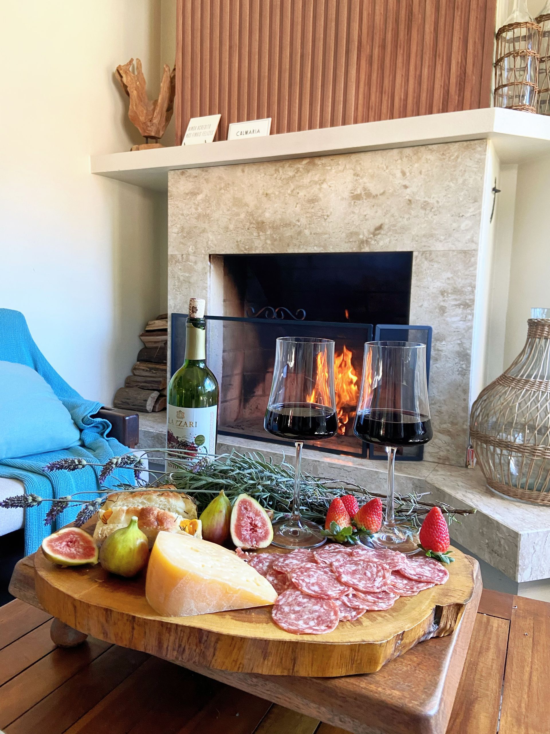 Uma tábua de corte de madeira com comida e vinho em frente a uma lareira.