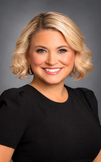 Smiling blonde woman in a black top against a gray studio background