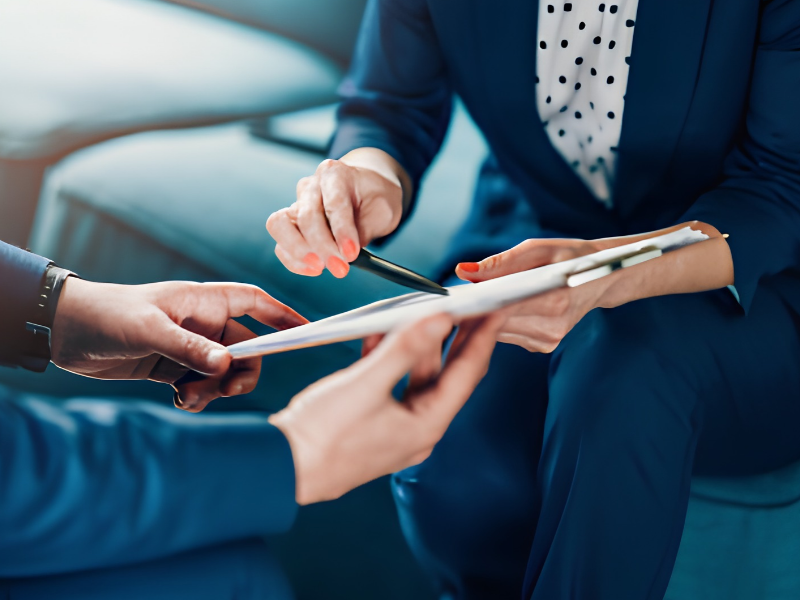 Two people in blue suits reviewing documents with a pen in a business meeting.