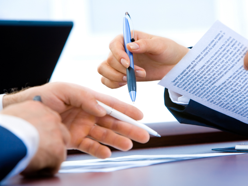 Hands exchanging a blue pen and paperwork at a desk during a business meeting