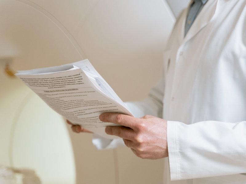 Person in a white coat holding and reading a document indoors
