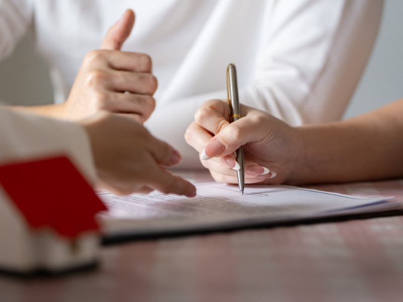 Hands gesturing over a form as someone signs with a pen at a desk