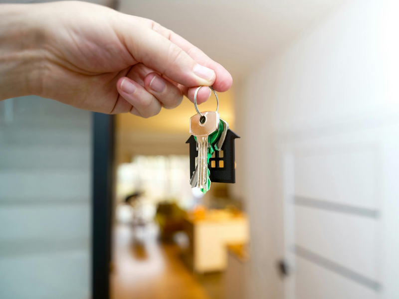 Hand holding a keychain with a small figurine, blurred indoor hallway in the background