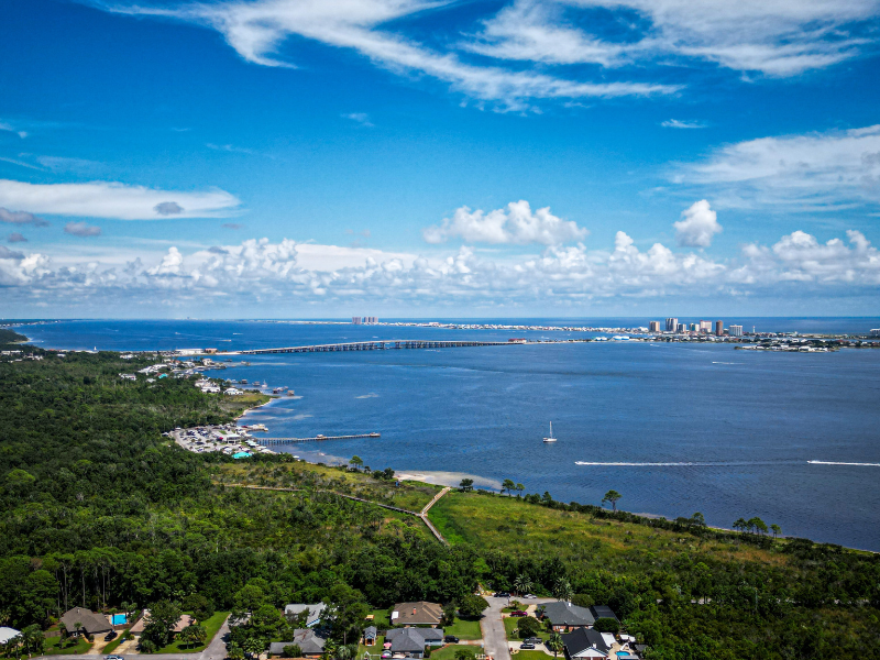 Wide coastal bay under blue sky, with green hills and a distant city skyline.