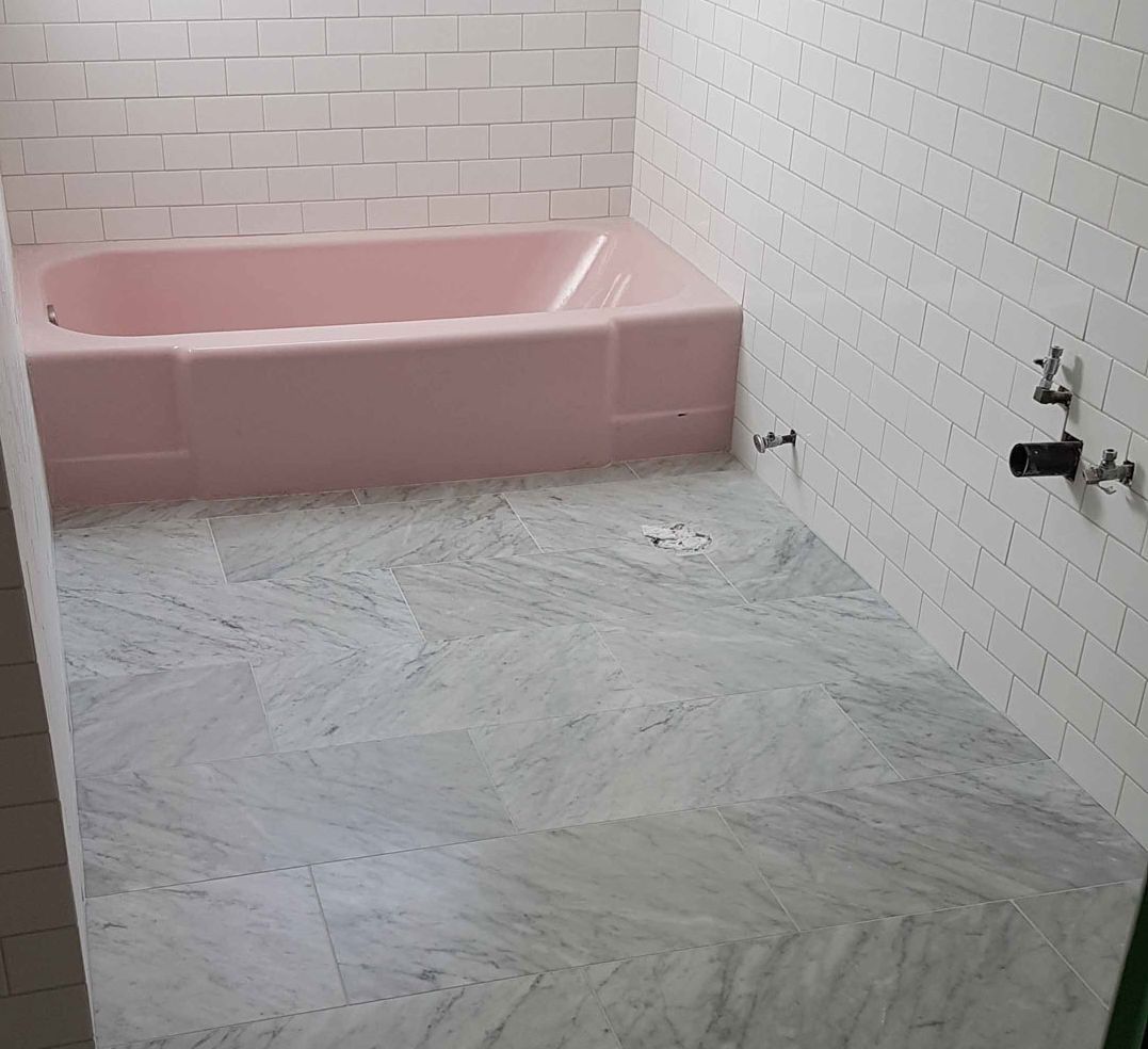 Baignoire rose dans une salle de bains carrelée avec sol et accessoires muraux en marbre gris.
