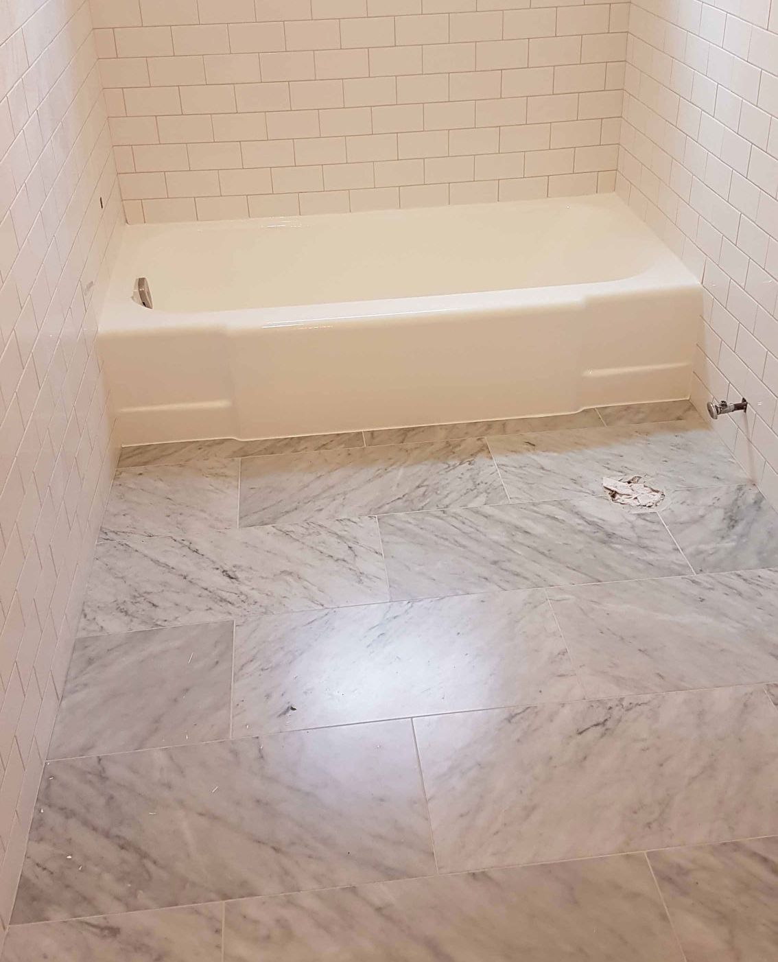 Salle de bain vide avec baignoire crème et sol en carrelage de marbre gris.