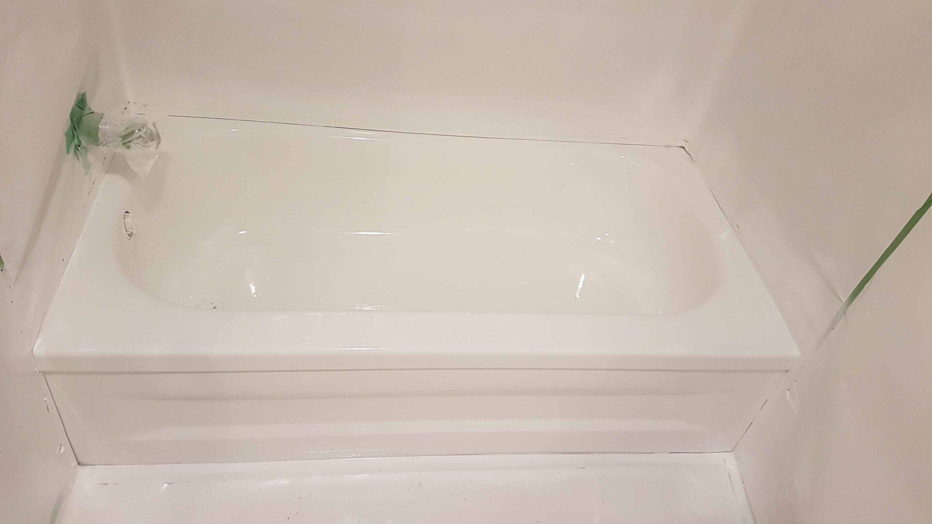 Baignoire blanche installée dans une alcôve de douche carrelée, avec une petite tache de peinture ou de mastic vert près du coin gauche.