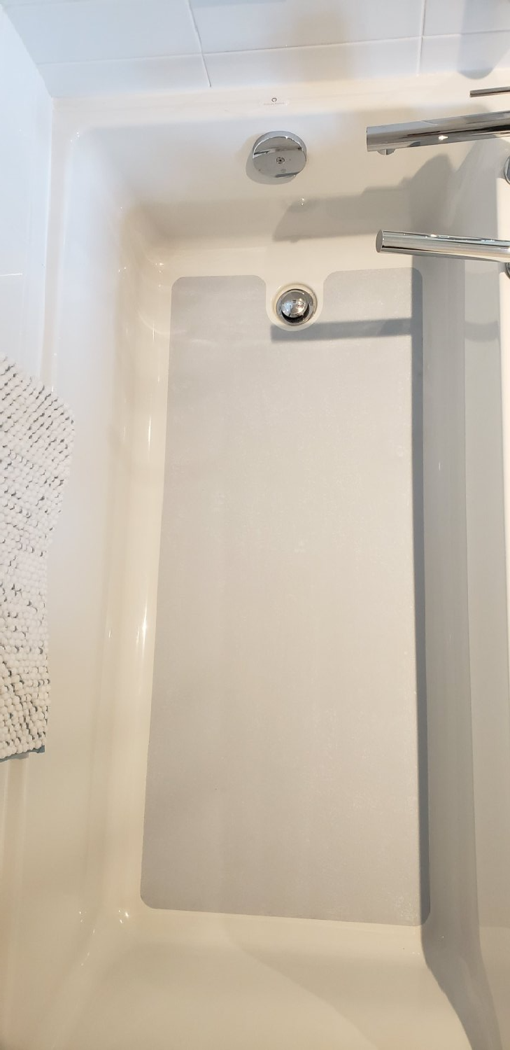 Baignoire/douche blanche avec robinetterie argentée et pommeau de douche à main sur un mur carrelé.