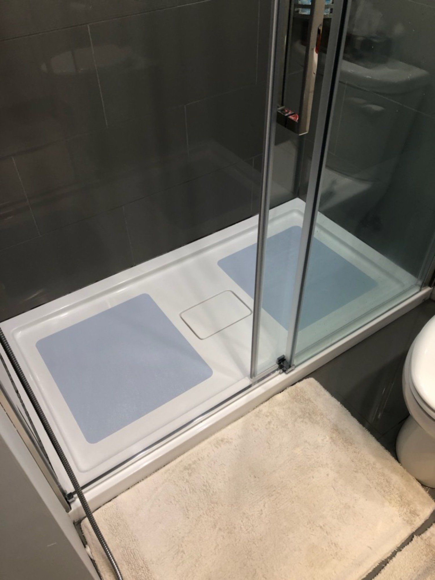 Petite salle de bain avec douche, porte en verre, tapis de bain beige et tapis antidérapant bleu clair à l'intérieur.