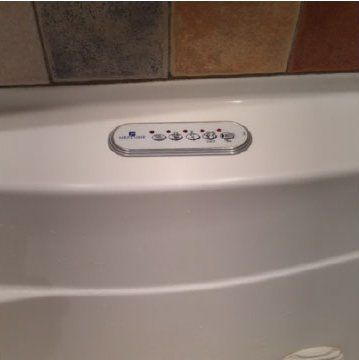 Baignoire blanche avec panneau de commande intégré sous le carrelage mural.