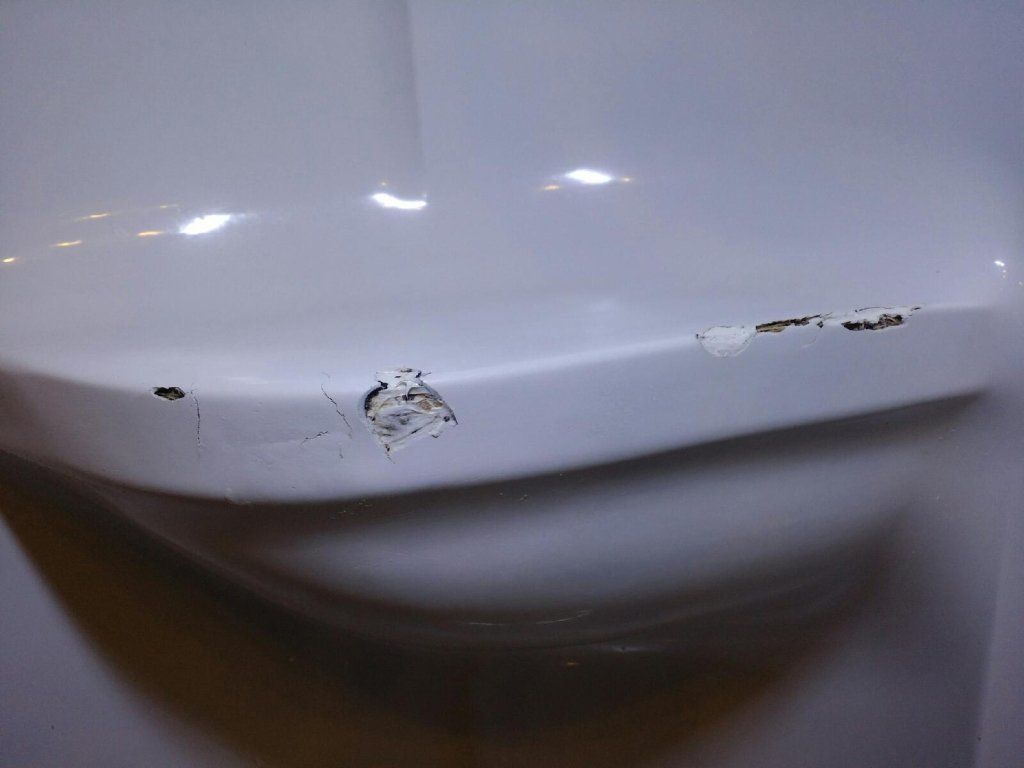 Gros plan sur un appareil électroménager blanc dont la peinture est écaillée et qui présente de petites taches de rouille sur le bord inférieur.