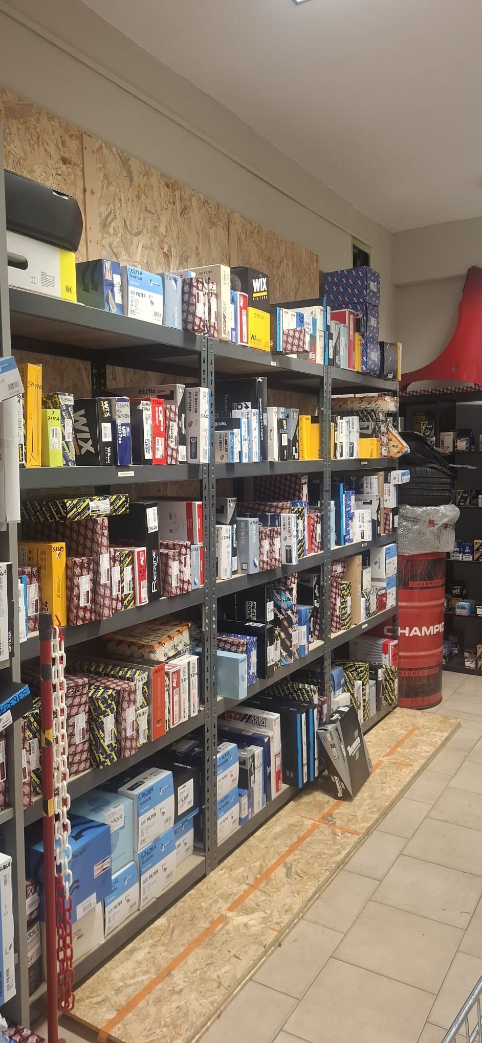 Scaffali pieni di giochi da tavolo e libri in uno stretto corridoio di un negozio con pavimento piastrellato e decorazioni murali.
