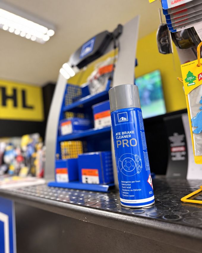 Scaffale di bottiglie di olio motore accanto a un contenitore arancione della Repsol, contro una parete gialla.