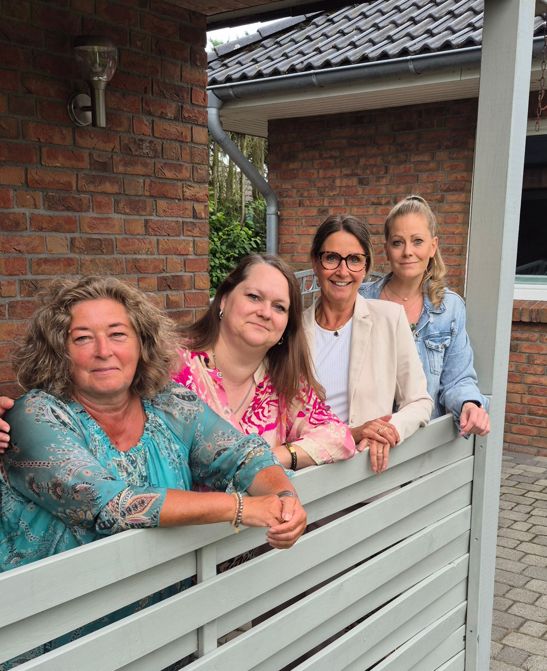 En gruppe kvinder står ved siden af hinanden på en veranda.