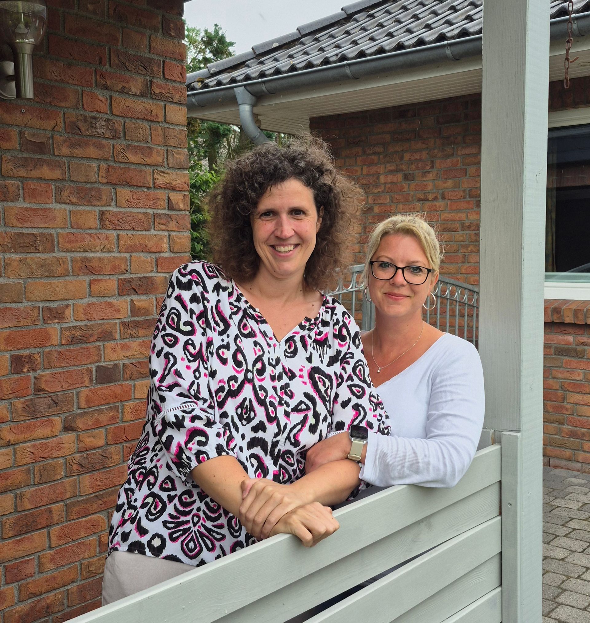 To kvinder poserer til et billede foran en murstensbygning