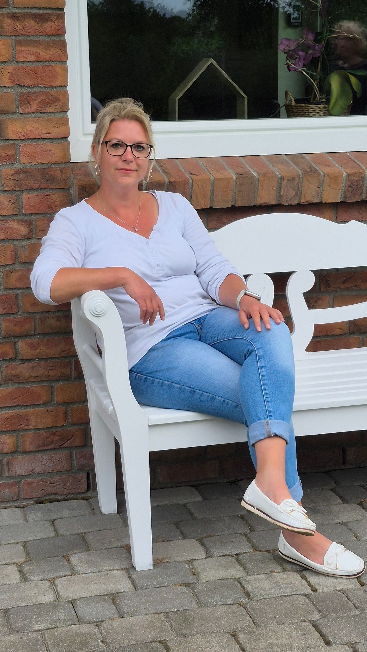 En kvinde sidder på en hvid bænk foran en murstensbygning.