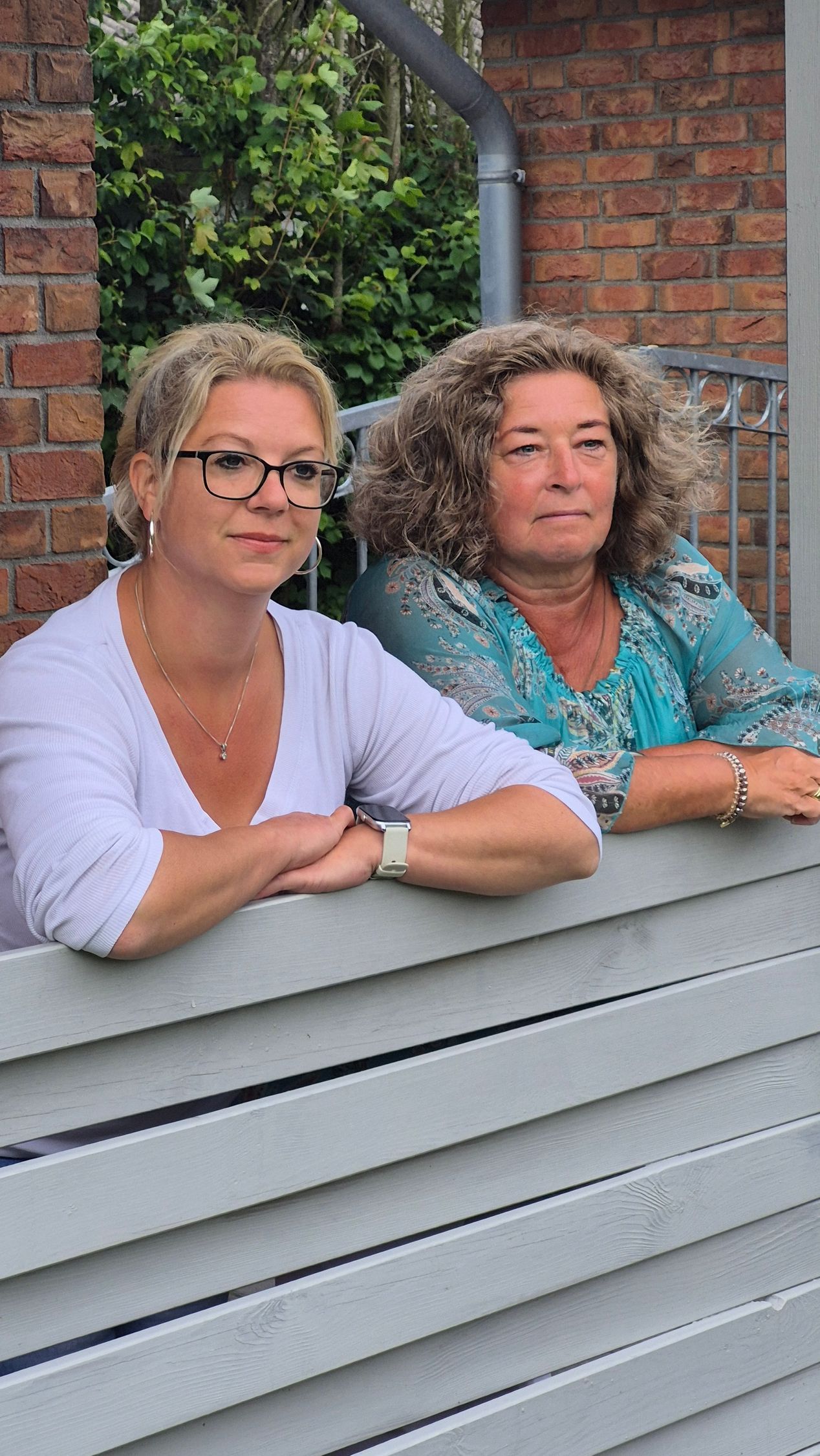 To kvinder læner sig op ad et træhegn.