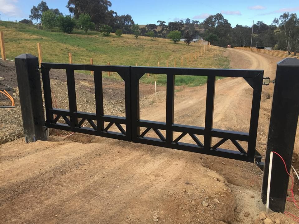 A black gate is sitting on the side of a dirt road.