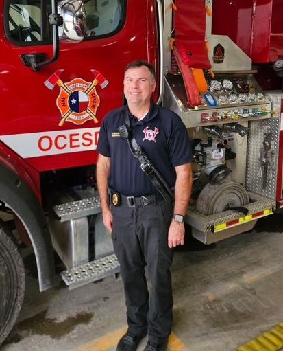 A man standing in front of a red Orange County fire tanker truck