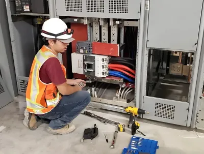 OE Services LLC - A man is kneeling down in front of a electrical cabinet.