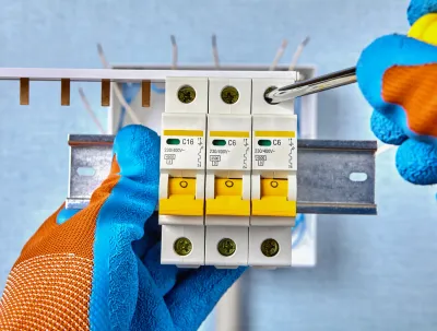 OE Services LLC - A person is holding a circuit breaker with a screwdriver.