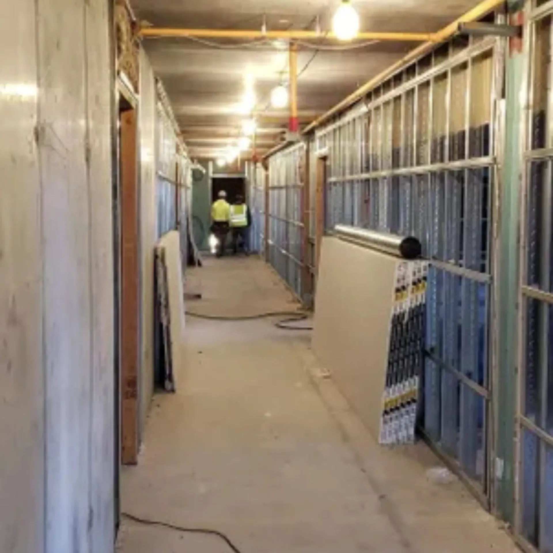 OE Services LLC - A long hallway in a building under construction with two men in yellow vests.